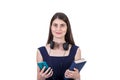 Trendy student girl with headphones around her neck holding a book and her smartphone in hands, looking contented to camera Royalty Free Stock Photo