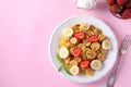 Trendy tiny pancakes for breakfast with strawberry, banana and sour cream in white plate on pink background. View from above. Copy Royalty Free Stock Photo