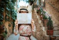 Trendy tourist woman in old Europe town hiding behind map