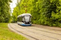 Trendy tram blue white runs along the rails in the park. Green foliage, modern city ecological transport tram, background