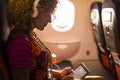 Caucasian woman seat inside the aircraft and use modern internet connected tablet device and headphones - concept of people and