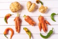 Trendy ugly curved vegetables - potato, carrot and chilli pepper on white wooden background