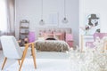 Vintage armchair in cute bedroom interior with black and white poster and king size bed with satin bedding