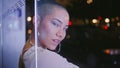 Trendy woman posing nightlights closeup. Beautiful bald girl at bus station.