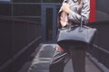 Trendy woman in silver pants jacket with black bag in hand street look. Fashionable outfit