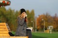 Trendy woman in stylish coat sitting on the bench in city park. Royalty Free Stock Photo