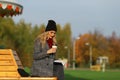 Trendy woman in stylish coat sitting on the bench in city park. Urban scene outdoors. Royalty Free Stock Photo