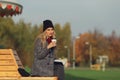 Trendy woman in stylish coat sitting on the bench in city park. Urban scene outdoors. Drinking takeaway coffee and writing or draw Royalty Free Stock Photo