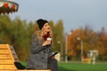 Trendy woman in stylish coat sitting on the bench in city park. Royalty Free Stock Photo