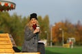 Trendy woman in stylish coat sitting on the bench in city park. Young beautiful woman smiling. Royalty Free Stock Photo