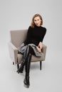 Trendy woman in turtleneck and ittle skirt sitting in armchair in studio and looking condescending