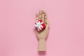 Trendy wooden mannequin hand holds small red gift box on pastel pink background, copy space, flat lay. March 8th, February 14th,