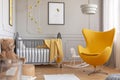 Trendy yellow egg chair in elegant grey nursery with wooden crib and posters on the wall Royalty Free Stock Photo