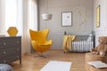 Trendy yellow egg chair in elegant grey nursery with wooden crib and posters on the wall Royalty Free Stock Photo