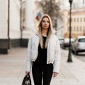 Trendy young blonde woman in black-white fashionable clothes with a leather stylish bag walks along the street on a warm  autumn Royalty Free Stock Photo