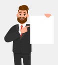 Trendy young business man showing blank white poster and pointing finger. Happy hipster person holding empty banner. Royalty Free Stock Photo