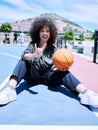 Trendy young hispanic woman making the rock gesture with her hands and fingers, holding a basketball on the court. Happy Royalty Free Stock Photo