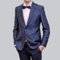 Trendy young man wearing blue blazer and tie bow, standing against a grey background Royalty Free Stock Photo