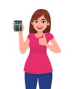 Trendy young woman showing, holding calculator and gesturing thumbs up sign. Modern stylish girl making like, good or positive. Royalty Free Stock Photo