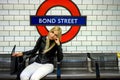 Trendy young woman sitting on a platform bench at Bond Street and waiting for an underground in London, England