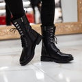 Trendy young woman stands on a tile in store in black cool leather lace-up boots with vintage jeans. Close up of female legs in Royalty Free Stock Photo