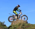 Trial motorcyclist standing on bike on rock silhouette against blue sky