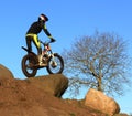 Trial motorcyclist standing on bike silhouette against blue sky