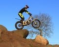 Trial motorcyclist standing on bike silhouette against blue sky