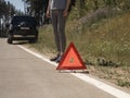 Triangle caution sign close up on road after car breakdown and female driver standing nearby Royalty Free Stock Photo