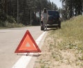 Triangle caution sign closeup on road with young woman going to car on background, waiting for emergency repair service Royalty Free Stock Photo