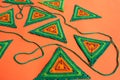 Triangle crochet patterns in green and orange colors and a green crochet cord on bright orange background.