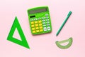 Triangle, protractor, pen and calculator are green on a pink background. A set of school supplies