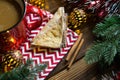 Triangular cookies with powdered sugar and cinnamon on a napkin with a zigzag pattern in the Christmas decor. Red coffee mug with
