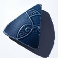 A triangular, dark blue ceramic shard featuring embossed geometric patterns rests Royalty Free Stock Photo