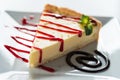 Triangular piece of cheesecake on a white plate decorated with mint and berry jam.