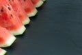 Triangular pieces of water melon arranged on black in line with copy space Royalty Free Stock Photo