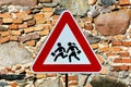 Triangular warning `children crossing` school road traffic sign with stone masonry wall behind Royalty Free Stock Photo