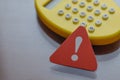 Triangular warning sign in foreground with blurred calculator behind, representing calculation error or financial caution Royalty Free Stock Photo