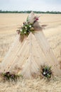 A triangular wooden arch, decorated with flowers, stands in a golden, mown field. Place for a wedding ceremony in rustic style in Royalty Free Stock Photo