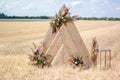 Triangular wooden arch decorated with flowers in a wheat field. A place for a wedding ceremony in the countryside. Rustic style Royalty Free Stock Photo