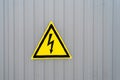 Triangular yellow sign of dangerous electrical voltage on the gray wall. Raindrop