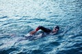 Triathlon athlete swimming on lake in sunrise wearing wetsuit