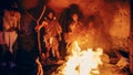 Tribe of Prehistoric Hunter-Gatherers Wearing Animal Skins Stand Around Bonfire Outside of Cave at Royalty Free Stock Photo