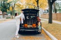 Trick or trunk. Halloween in car. Woman decorating vehicle for traditional October holiday outdoor. Red pumpkins, scarecrow, Royalty Free Stock Photo