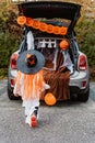 Trick or trunk. Trunk or treat. Little child in Halloween witch hat walk to decorated trunk of car for candies.