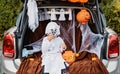 Trick or trunk. Trunk or treat. Happy child in ghost costume having fun celebrating Halloween party in decorated trunk of car