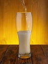 a trickle of light beer flows into a glass glass, beer with a thick rising white foam. wooden background.