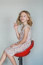 Cute European teen girl on a gray background sitting on a red chair. beautiful curly blonde with white teeth. an expressive smile