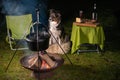 Tricolor Australian Shepherd dog sits next to a campfire and table with food and drink. At the campsite at night in