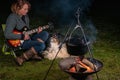 A tricolor Australian Shepherd looks at a woman playing guitar. At night by the campfire in a remote place. Camping in Royalty Free Stock Photo